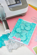 Card with decorative cutouts and 'smile' text on a pink surface with crafting tools.