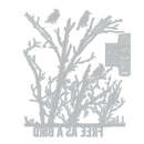 A gray metal die-cut stencil or craft sheet featuring bare tree branches with three birds perched on them, plus the words 'FREE AS A BIRD' and 'AS A BIRD' in a vertical banner, shown on a plain white background.