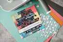 A handmade layered card featuring a colorful abstract design with the text 'FILLED WITH WONDER', displayed alongside crafting tools and papers on a textured mint green mat.