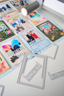 A close-up of a crafting workspace showing a metal die-cut frame with the word 'MERRY' and other silver metal frame dies scattered on a white surface, alongside sample photo cards and a white rotary cutter.