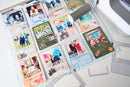 A collage of scrapbook paper sheets with colorful photos, decorative text, and craft elements laid out on a white surface, with a die-cutting machine partially visible at the top right.