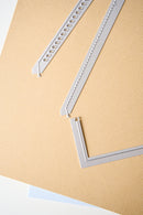 Three light gray metal embossing or cutting dies arranged diagonally on a textured beige sheet, with a small piece of light blue paper visible at the bottom edge.