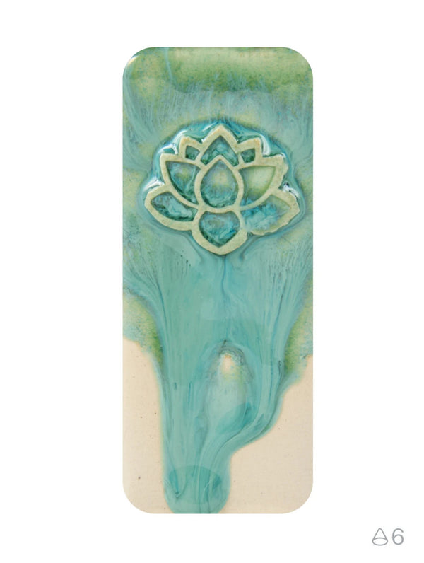 A rectangular ceramic tile with rounded corners, featuring a glossy teal and light green marbled design with a raised lotus flower motif near the top, set against a plain white background.