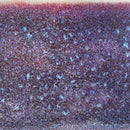 A close-up texture shot of a dark brown and purple speckled material with light blue flecks, resembling a mottled fabric or textured paper.