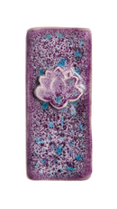A rectangular ceramic tile with rounded corners, featuring a textured purple and white speckled glaze with small blue accents, and a raised white lotus flower motif in the center.