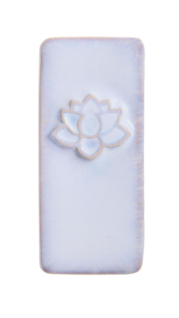 A rectangular ceramic tile with rounded corners, featuring a raised lotus flower motif in the center. The tile has a light lavender-blue glazed surface with subtle warm beige edging and a white lotus design.
