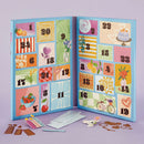 An open advent calendar with two blue panels showing numbered illustrated compartments, displayed on a lavender background with small decorative cutouts and envelopes in front.