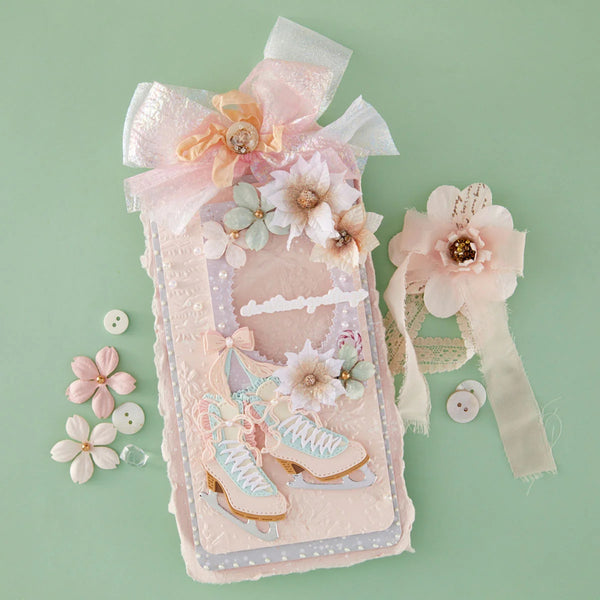 A decorative pastel pink phone case with a bow, floral embellishments, and ice skates, displayed on a mint green background with matching flower accessories.