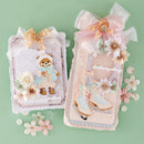 Two decorative handmade card or album cover designs displayed on a mint green background. The left design features a teddy bear in winter clothing with white and pale pink embellishments, and the right design shows ice skates with pale pink, white, and light blue embellishments.