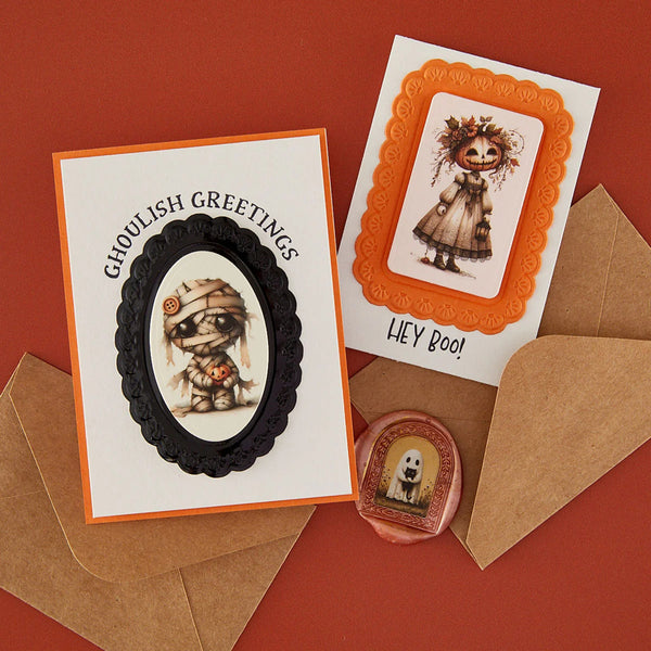 Two Halloween greeting cards with orange and black borders, displayed with brown envelopes on a red background. One card shows a mummy illustration with the text 'Ghoulish Greetings,' and the other shows a ghostly figure with the text 'HEY BOO!'.