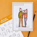 A greeting card featuring a hand-drawn family of four wearing red Santa hats, displayed on an orange textured background alongside a stamp booklet and a pencil.