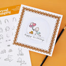 A handmade square birthday card with a white center, scalloped brown border, and a cartoon baby holding pink and red balloons with the words 'happy birthday,' shown on an orange background with stamp sheets and a pencil nearby.