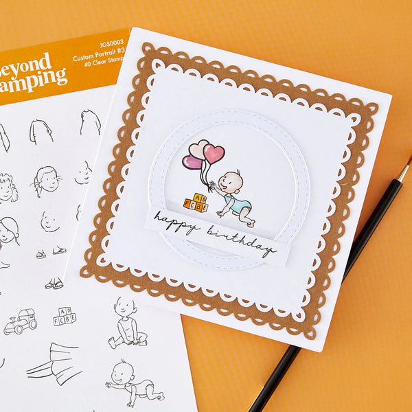 A handmade square birthday card with a white center, scalloped brown border, and a cartoon baby holding pink and red balloons with the words 'happy birthday,' shown on an orange background with stamp sheets and a pencil nearby.