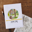 A white greeting card with a circular watercolor illustration of a cabin in a forest and the text 'LIVIN' THE D.R.
