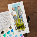 A printed card or journal page featuring a hand-drawn illustration of two men standing outdoors with the text 'DAYS like this' at the bottom, styled on a wooden surface with a pen, paint swatches, and die-cut sticker templates.