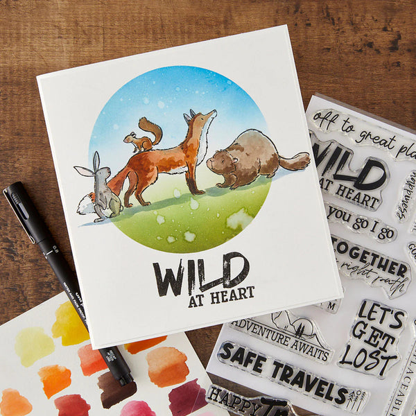 Card with animal illustration and 'Wild at Heart' text on a wooden surface with watercolor swatches and stamps.