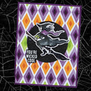 A square handmade greeting card with a purple border and a harlequin diamond pattern in purple, orange, white, and lime green. The center features a black circular background with a stamped witch riding a broomstick and the text 'YOU'RE WICKED COOL'.