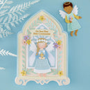 A decorative arch-shaped angel keepsake card or plaque on a light blue background, with a small angel figure shown beside it. The central item features a layered angel illustration in a blue dress, white wings, flowers, and the text 'On Your First Holy Communion.