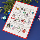 A square Christmas greeting card with a red border, featuring hand-drawn holiday ornaments and illustrations including a Santa Claus, snowman, teddy bear, candy cane, and hot chocolate. The card is displayed on a dark blue surface with green pine branches and colorful Christmas ornaments as props.