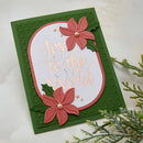 A handmade greeting card with a dark green textured border, a white central oval, and rose gold foil script reading 'Joy to the World'. The card is decorated with two pink poinsettia flowers and green holly leaves, accented with small pearl-like beads.