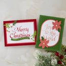 Two handmade Christmas greeting cards displayed on a light marble surface with holiday greenery and red berries. One card reads “Merry Christmas” in red script on a white background with a red border, and the other reads “Joy to the World” in gold script on a green polka-dot background with layered coral flowers and green leaves.