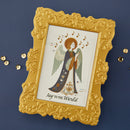 Decorative angel card with music notes and 'Joy to the World' text, framed in gold on a dark blue background.