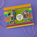 Colorful card with Christmas-themed design featuring elves and text on a purple background.