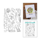Clear stamp set sheet with black line-art illustrations of trees, cabins, and outdoor scenes, shown alongside a printed card featuring a colorful cabin illustration and the stamped design on a wood surface.