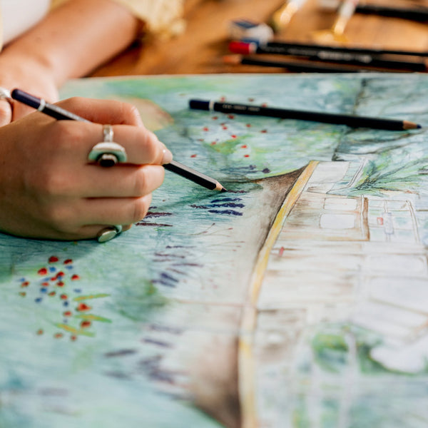 Person coloring a detailed illustration with colored pencils on a map.