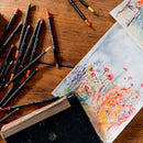 Art supplies including colored pencils and a watercolor painting on a wooden surface.