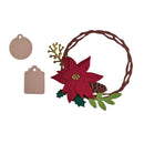 A Christmas wreath embellishment featuring a brown twisted wreath frame, a large red poinsettia flower with a gold center, green holly leaves, a pinecone, and gold decorative sprigs, shown alongside two blank beige tags on a white background.