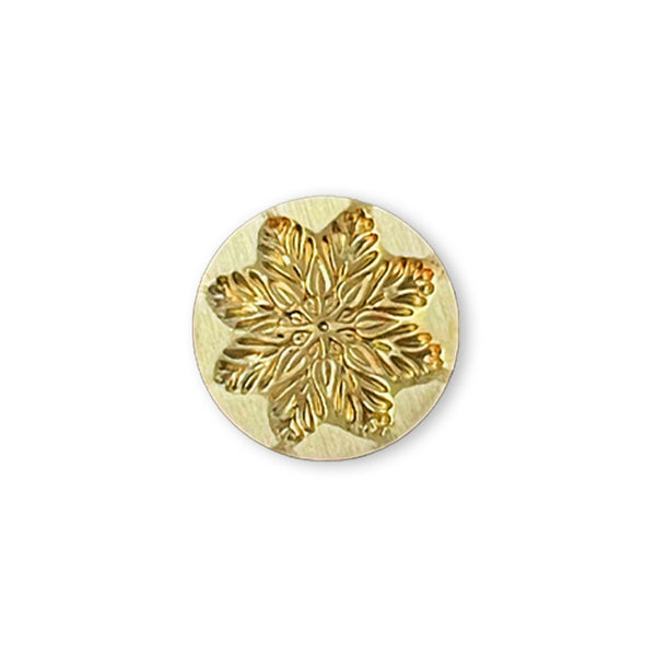 A round gold-toned metal stamp or mold featuring an embossed snowflake design, shown on a plain white background.