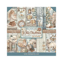 A square scrapbooking paper pack titled 'Amperia White Christmas' by Christine Mangiarotti, featuring 10 double-faced sheets with vintage holiday illustrations including a girl in a winter dress, lanterns, sheep, a goose, a puppy, and cozy Christmas houses. The packaging has a dusty blue border and shows the website www.