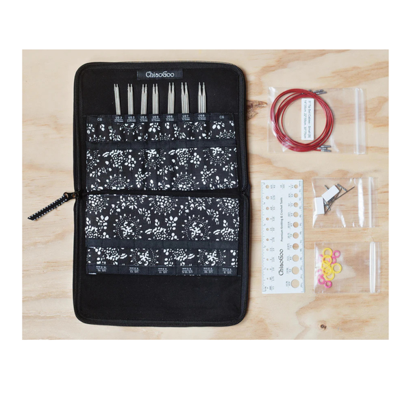 Black floral-patterned case with knitting needles and accessories on a wooden surface
