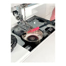 Close-up of a sewing machine interior with a pink cleaning brush being used to clean around the needle area, with a finger visible holding the brush.