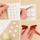 A four-panel collage showing white round adhesive dots/stickers being applied with tweezers and used to make a bow with a red ribbon, on a beige background.