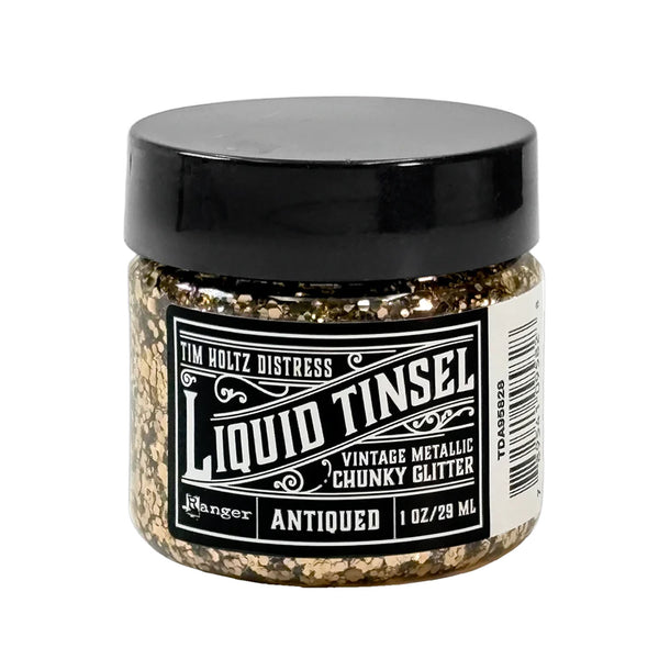 A jar of Tim Holtz Distress Liquid Tinsel chunky glitter in the 'Antiqued' shade, featuring a black lid and a black-and-white label, shown on a plain white background.
