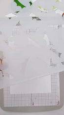 White layered paper cutout sheets with scalloped edges layered over a gray gridded cutting mat.