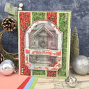 A handmade Christmas greeting card featuring a central grayscale photo of a snowy house door, surrounded by red poinsettia and green patterned borders. The card is styled on a rustic wooden surface with holiday ornaments, a pinecone, and a textured blue backdrop.