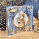 A handmade Christmas greeting card with a snowman illustration, decorated with blue borders, gold foil details, and festive holiday elements, displayed on a tabletop with a pinecone and gold wire decor.