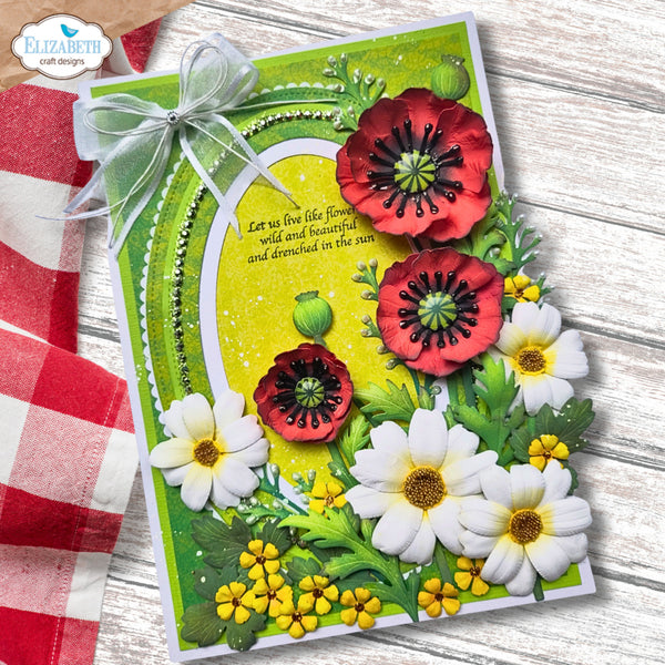 A handmade greeting card featuring layered 3D paper flowers in red, white, and yellow on a bright green background, tied with a sheer white ribbon. The card is displayed on a rustic white wood surface next to a red and white checkered cloth, with an 'Elizabeth craft designs' logo in the top-left corner.