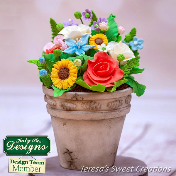Decorative flower pot with colorful flowers on a light background, featuring 'Katy Sue Designs' and 'Teresa's Sweet Creations'.