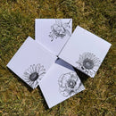 Five white cards with black floral illustrations on grass