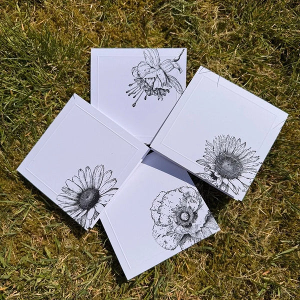 Five white cards with black floral illustrations on grass