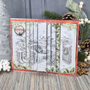 A handmade Christmas card with a red border and five vertical panels showing black-and-white winter garden scenes, styled on a rustic wood surface with holiday greenery and pinecones.