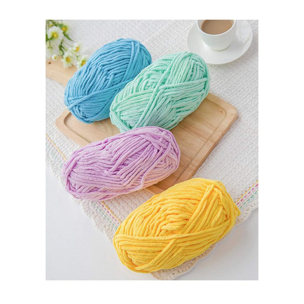 Four balls of yarn in blue, green, pink, and yellow on a wooden board with a cup of coffee in the background.
